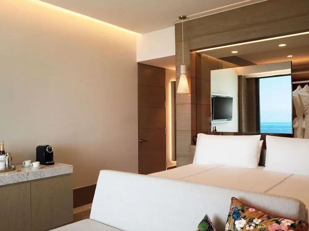 Helles Hotelzimmer mit Bett, kleiner Couch, Kaffeemaschine und Wandspiegel.