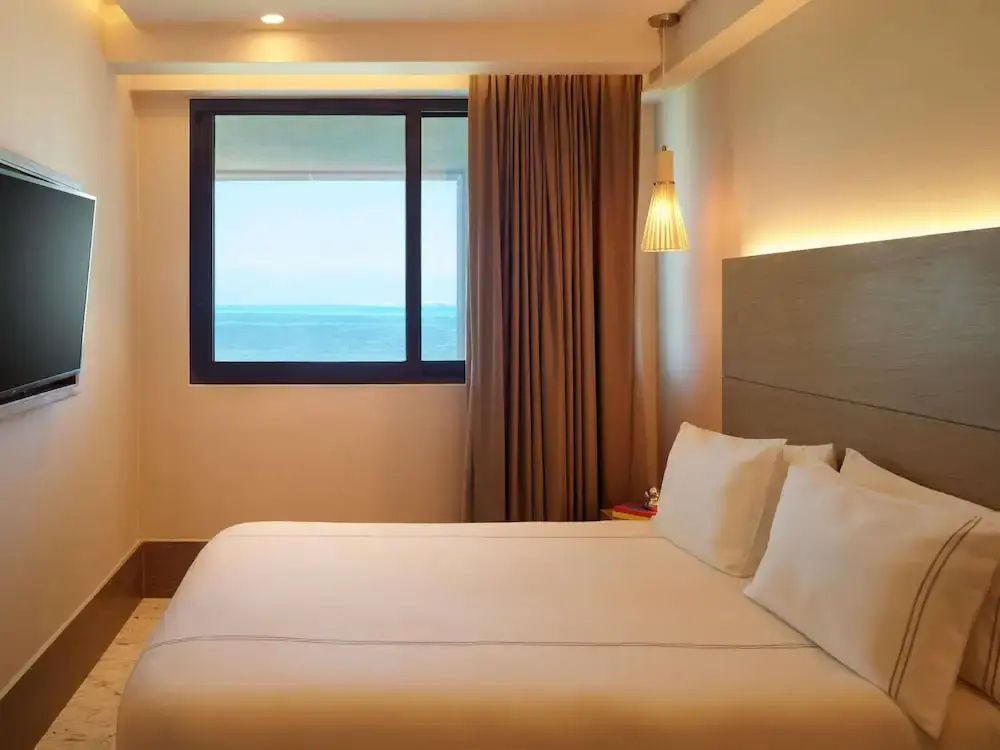 Doppelbett in hellem Zimmer mit Fenster und Blick auf das blaue Meer.