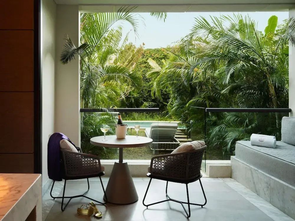 Überdachter Balkon mit Tisch, zwei Stühlen und Blick auf tropische Palmen sowie den Gartenbereich.