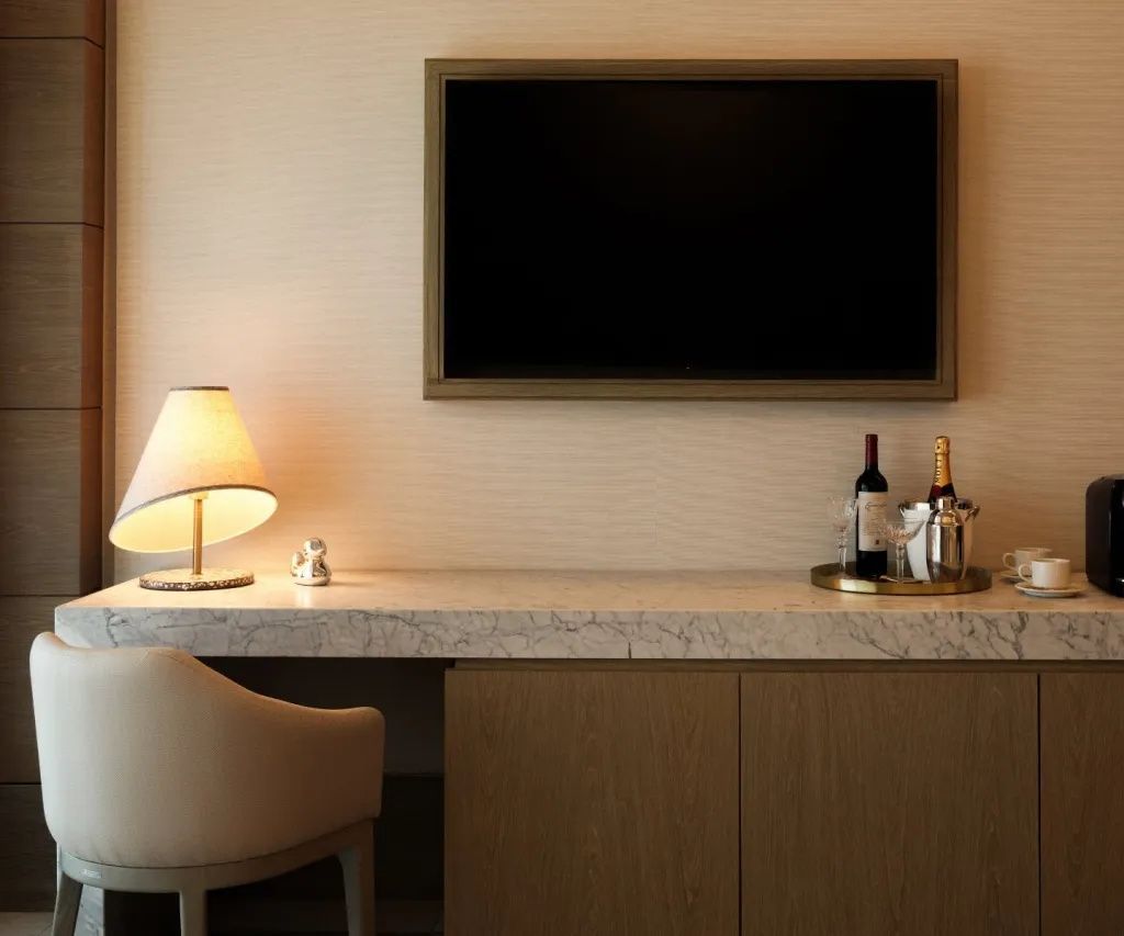 Arbeitstisch mit Marmorplatte, Wandfernseher, Lampe und Stuhl im Hotelzimmer.