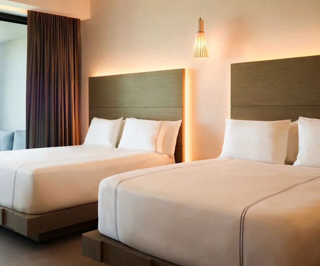Doppelzimmer mit zwei Betten, Holzkopfteilen und indirekter Beleuchtung an der Wand.