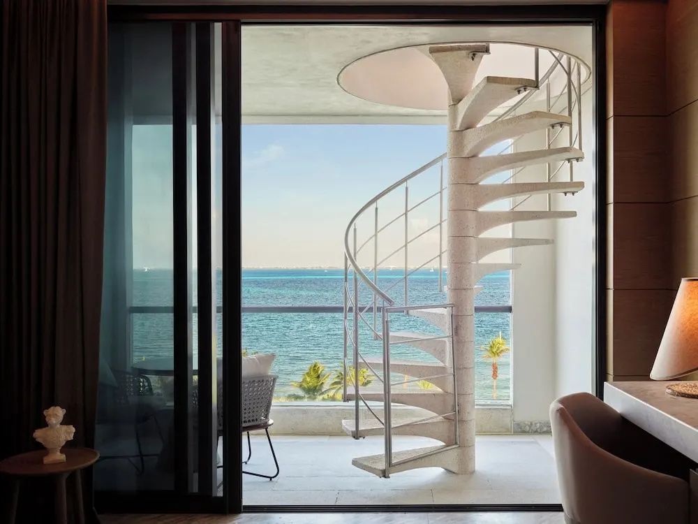 Balkon mit einer weißen Wendeltreppe und Panoramablick auf das Meer und Palmen.