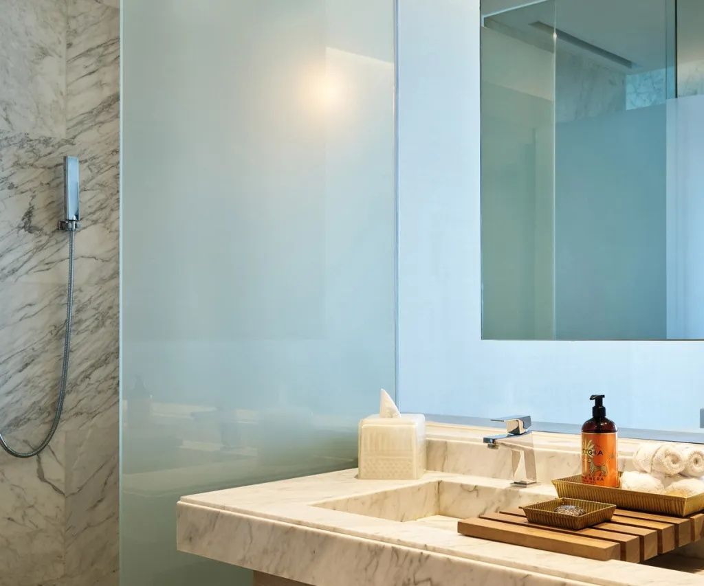 Waschtisch aus Marmor mit Waschbecken, Pflegeprodukten und einer Glaswand im Badezimmer.