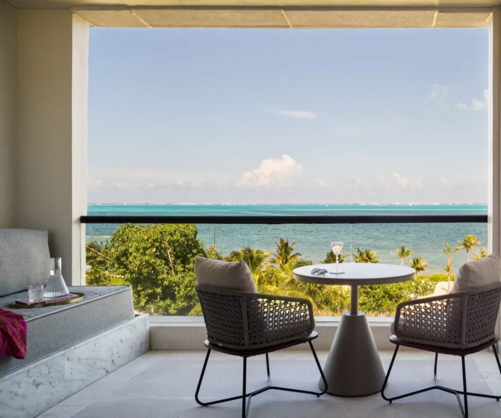 Balkon mit Sitzecke, Tisch und Ausblick auf grün bewachsene Küste und das Meer.