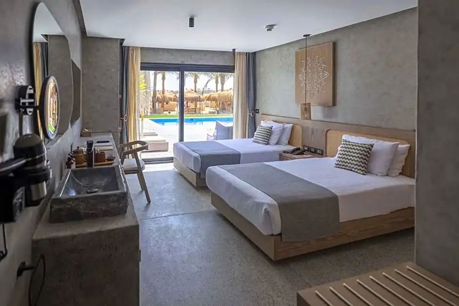 Hotelzimmer mit zwei Betten, Holzmöbeln und Terrasse mit Poolblick.