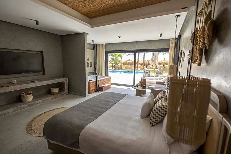 Schlafzimmer mit Doppelbett, Whirlpool und Glasfront mit Blick auf den Pool.