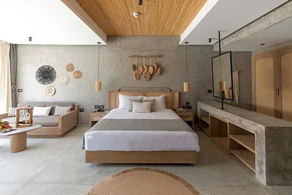Doppelbett mit hellen Kissen und Holzansatz vor grauer Wand im Hotelzimmer.