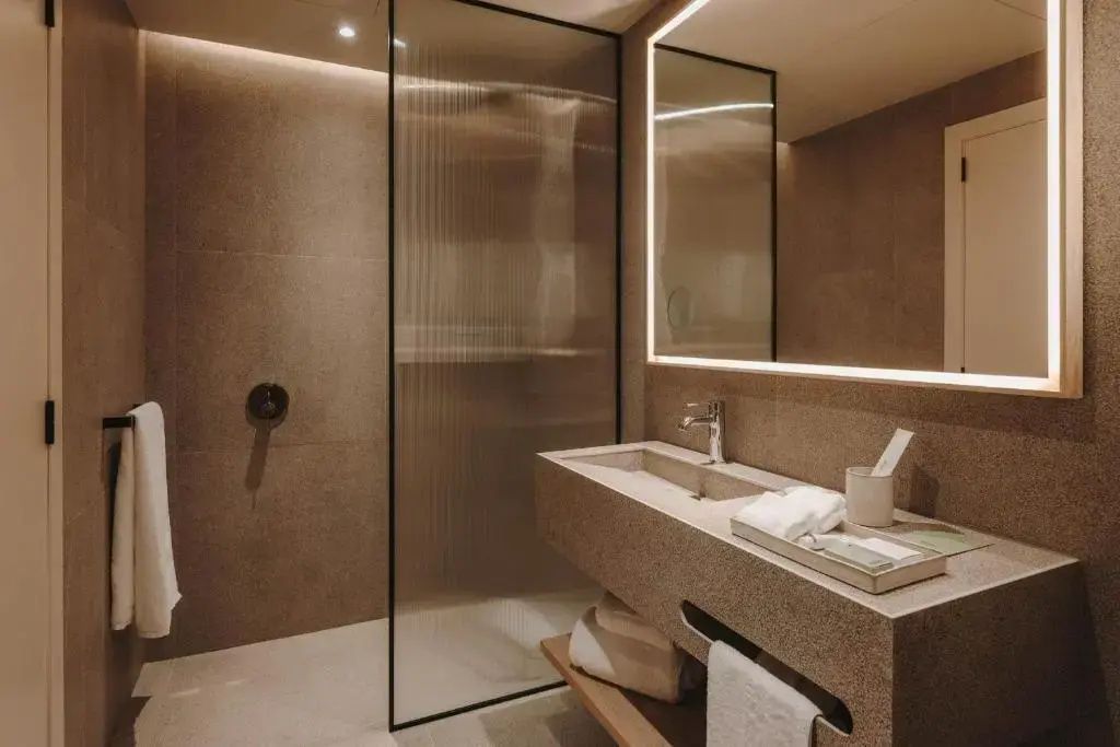 Modernes Badezimmer mit Waschtisch aus Stein, Spiegel und Dusche.