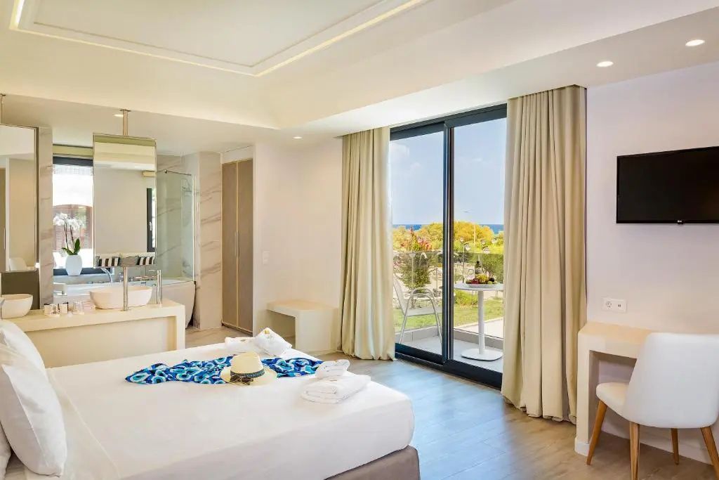 Helles Hotelzimmer mit Doppelbett und Balkontür mit Blick ins Grüne und auf das Meer.