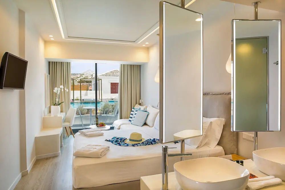 Zimmer mit Waschtisch im Vordergrund und Glasfront zum Poolbereich.