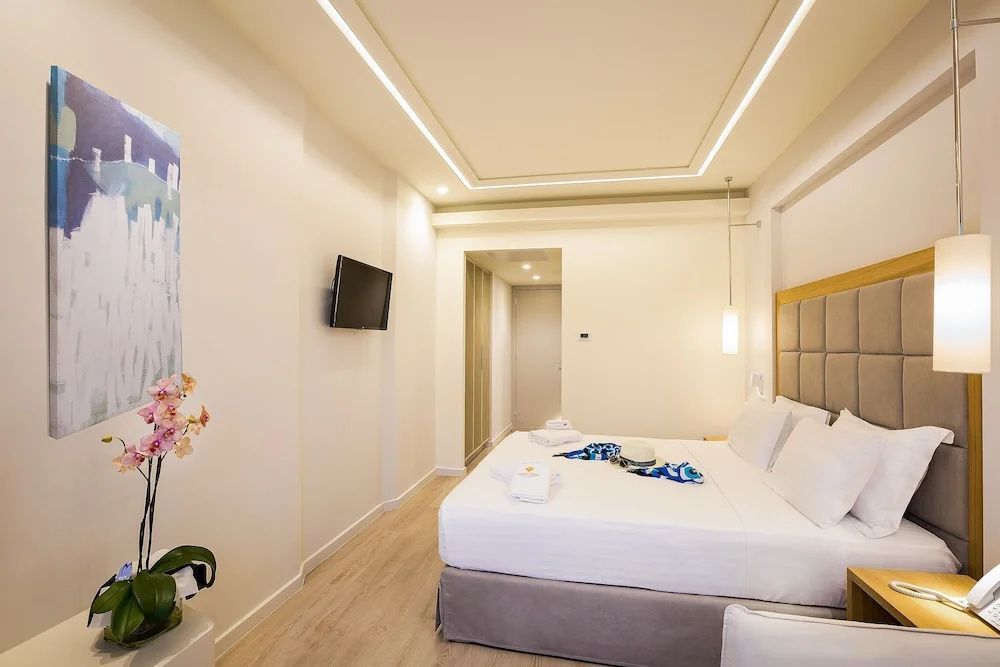 Schlafbereich eines Hotelzimmers mit großem Doppelbett, Wandfernseher und hellem Holzfußboden.