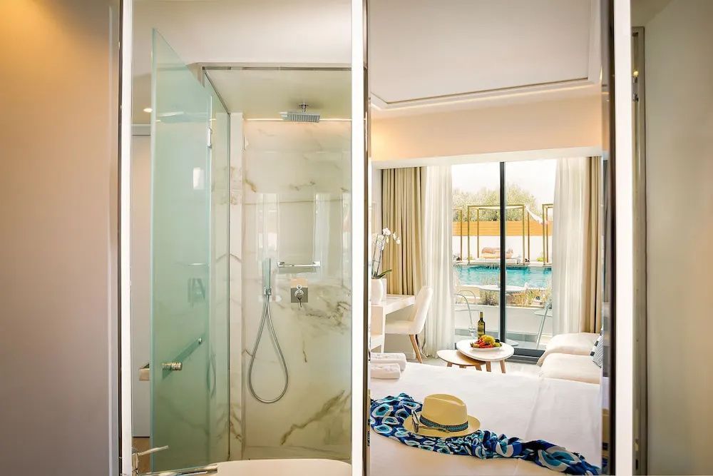 Blick in das Hotelzimmer mit angrenzendem Badezimmer mit Glasdusche und Terrasse zum Pool.