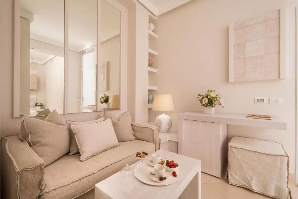 Heller Wohnbereich einer Suite mit beigefarbenem Sofa, Couchtisch und spiegelverkleideter Wand.