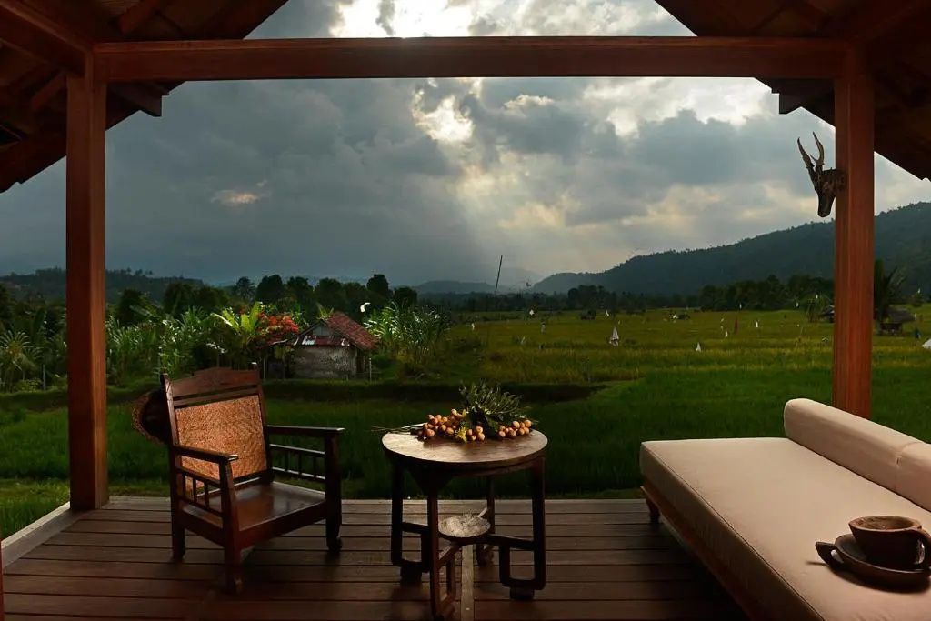 Terrasse mit Holzstuhl und Tisch bietet einen weiten Blick auf grüne Reisfelder.