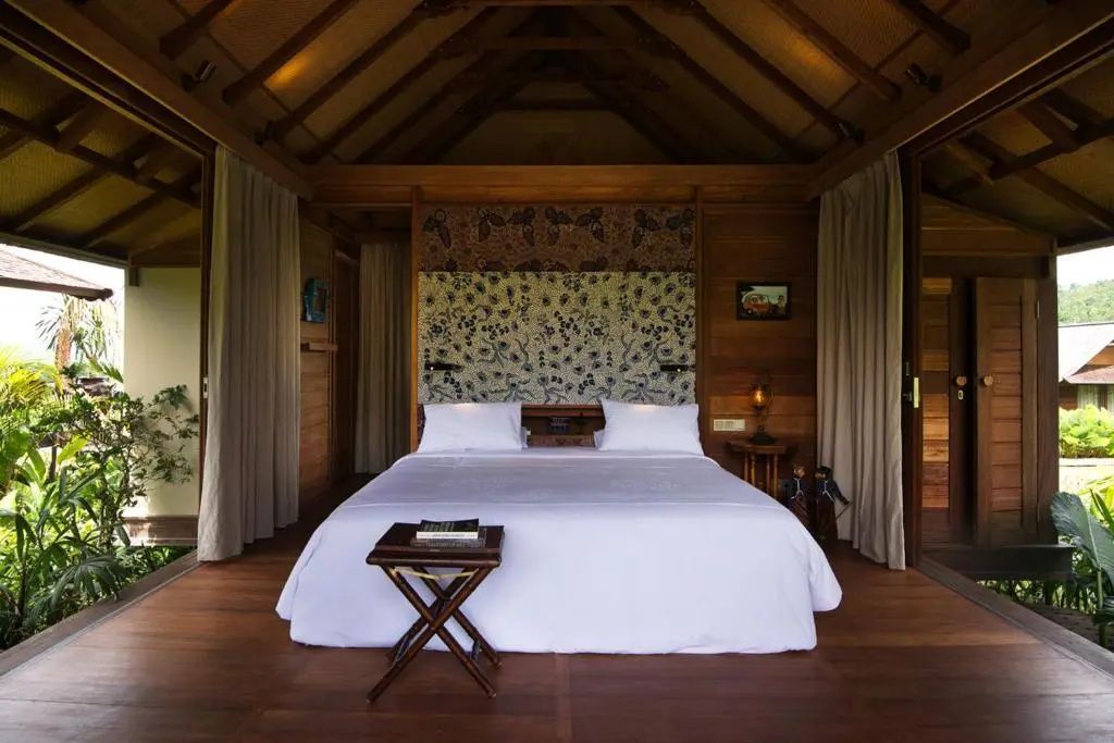 Schlafzimmer mit Holzverkleidung, Reetdach und großem Doppelbett mit musterüberzogener Rückwand.