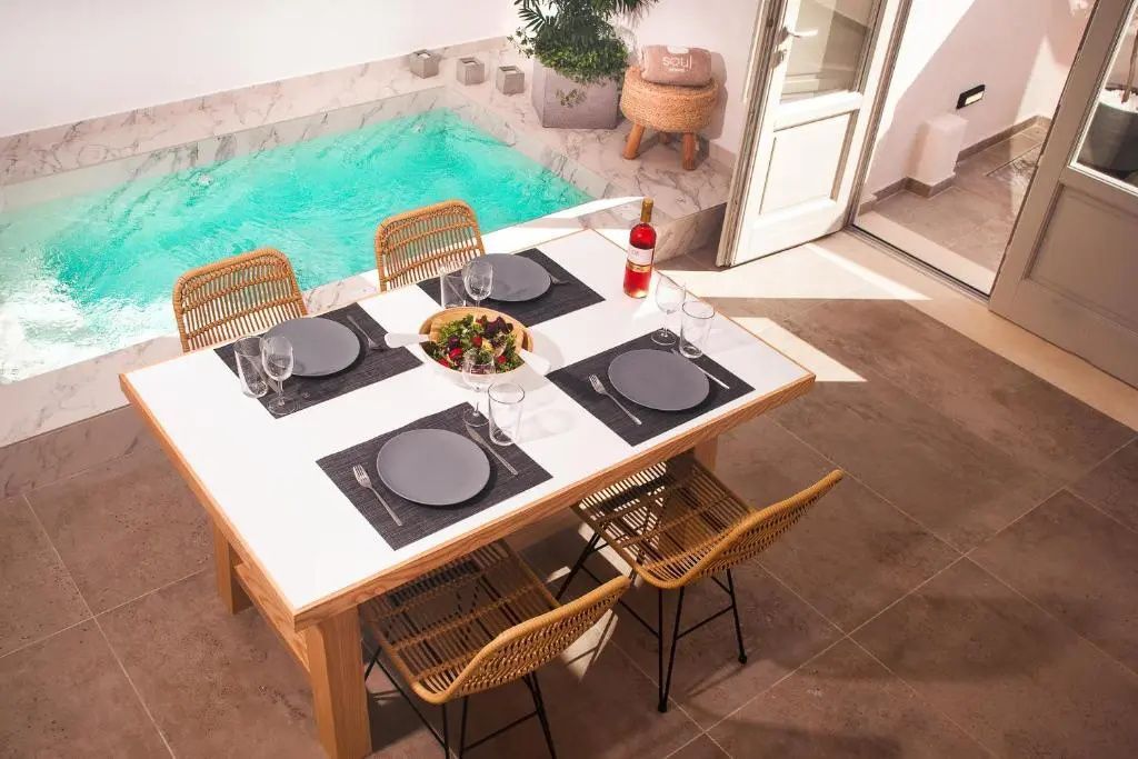Gedeckter Esstisch auf einer Terrasse mit Stühlen und kleinem Pool im Hintergrund.