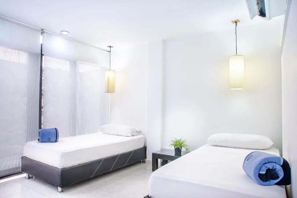 Hell gestaltetes Hotelzimmer mit zwei Einzelbetten und modernen Hängelampen.