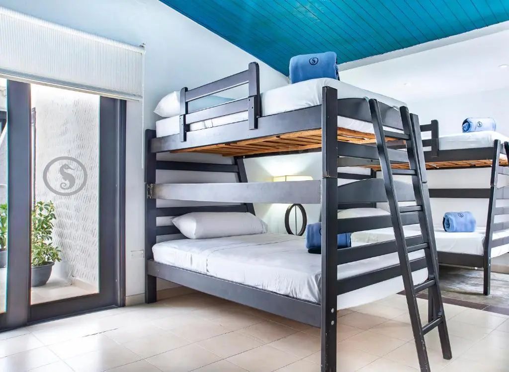 Etagenbett aus dunklem Holz in einem hellen Zimmer mit blauer Holzdecke.