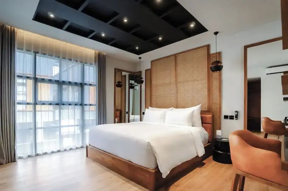 Doppelbett im Hotelzimmer mit hoher Holzrückwand, Kassettendecke und Balkontür.