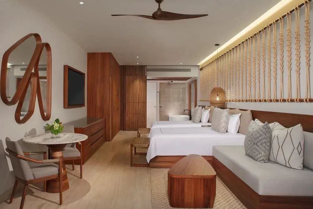 Hell eingerichtetes Hotelzimmer mit zwei Betten, Holzmöbeln und modernem Deckenventilator.