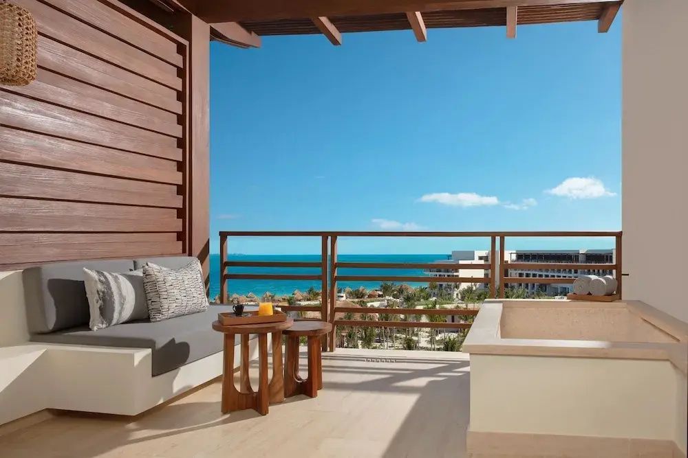 Balkon mit Sitzgelegenheit und Holzgeländer sowie Blick auf das Meer und die Anlage.