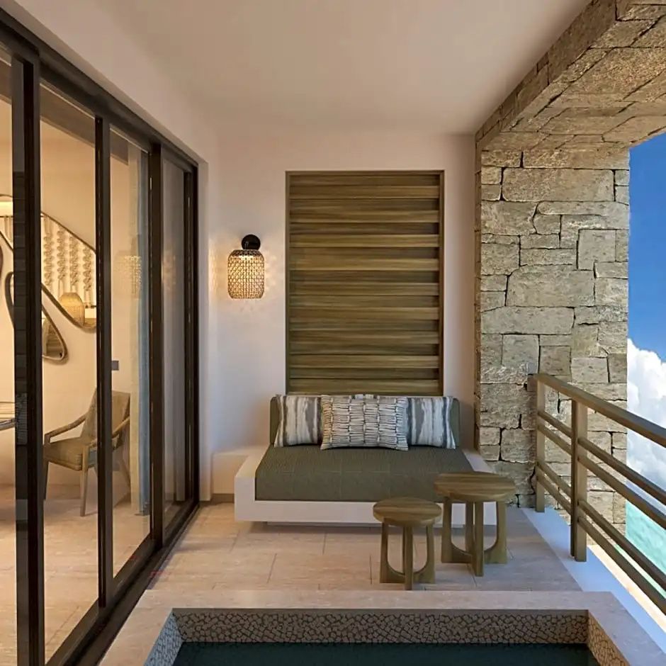 Balkon mit gepolsterter Sitzgelegenheit, Holztischen und einer Steinwand neben der Schiebetür.