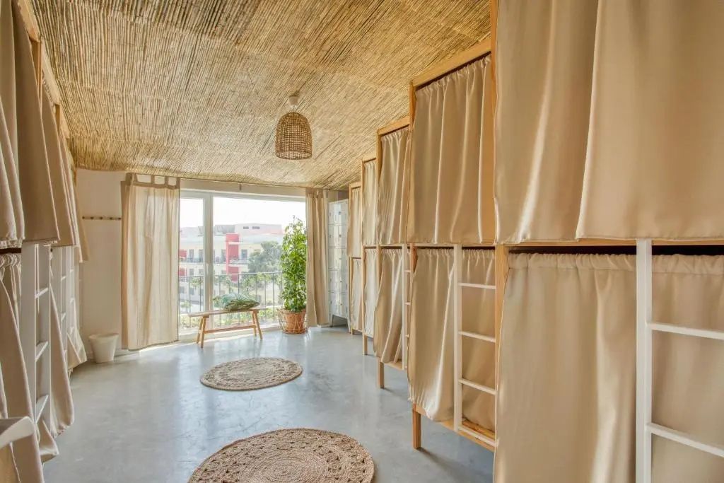 Mehrbettzimmer mit hölzernen Etagenbetten, Vorhängen und Vorlegern auf Estrichboden