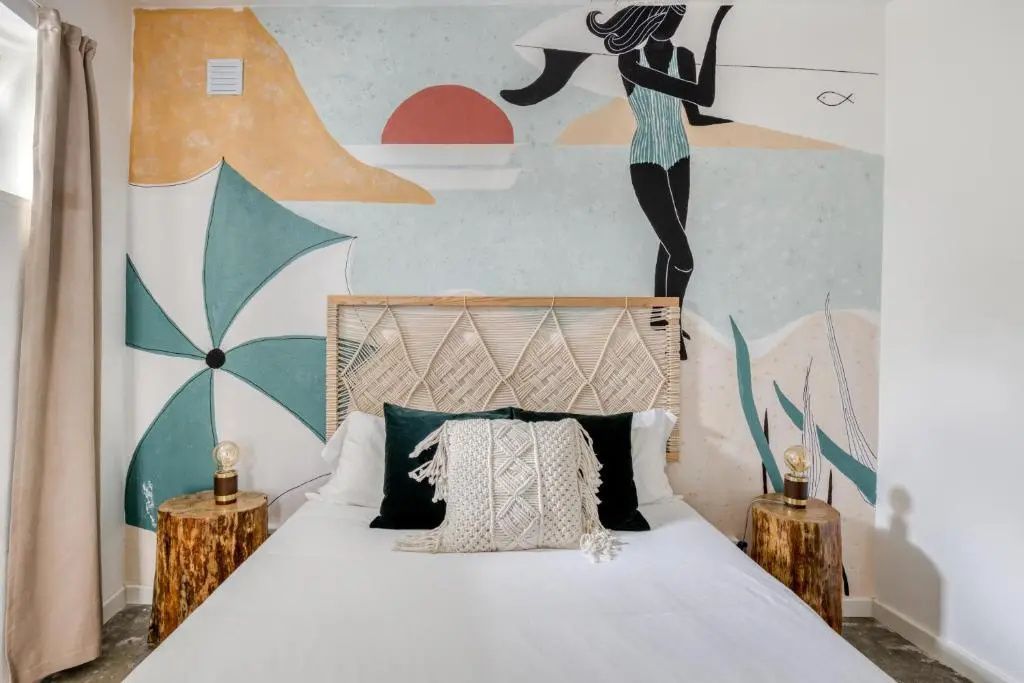 Doppelbett mit geflochtenem Kopfteil und Wandbild mit Surfmotiv sowie Nachttischen aus Holz