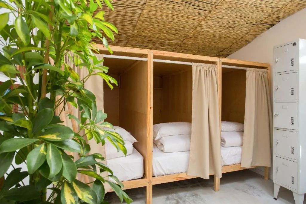 Holzbetten in einem Mehrbettzimmer mit weißer Bettwäsche und beigen Vorhängen