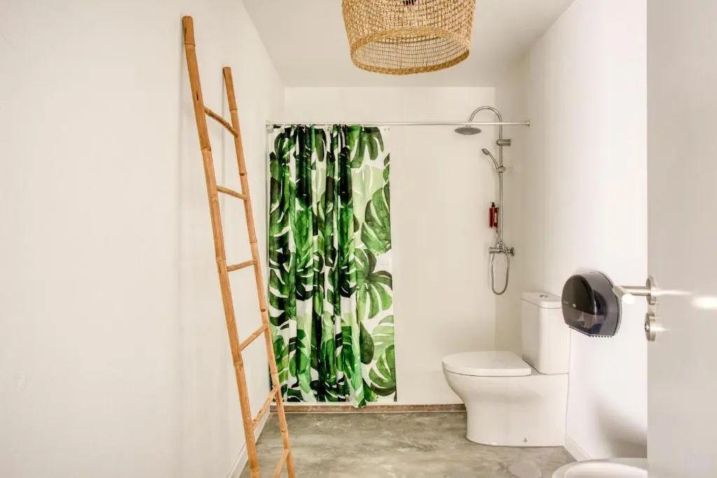 Badezimmer mit Toilette, Dusche mit grün gemustertem Vorhang und einer Anlehnleiter aus Holz.