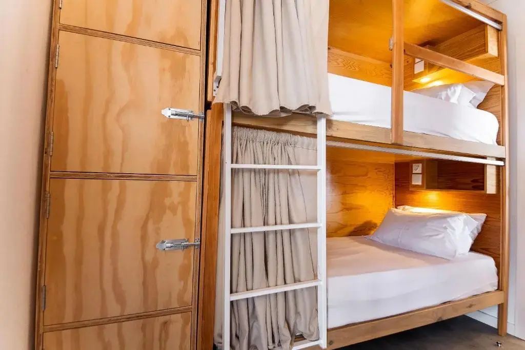 Etagenbett aus Holz mit beige Vorhängen zum Zuziehen und einer Leiter für das obere Bett.