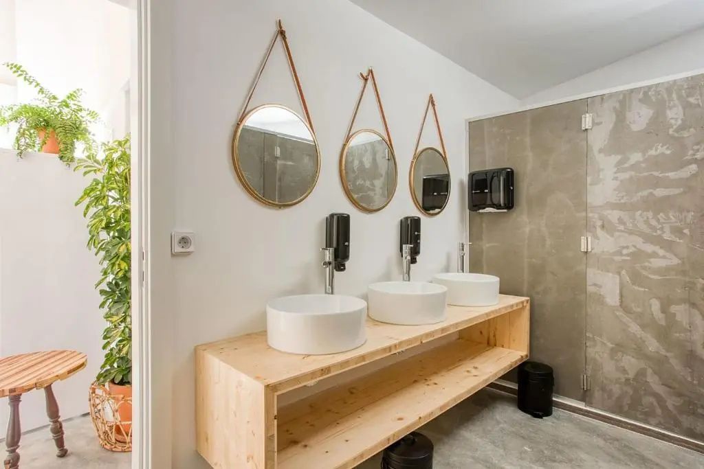 Waschtisch aus Holz mit drei runden Waschbecken und hängenden Spiegeln an der weißen Wand.