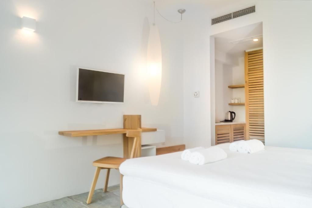 Helles Hotelzimmer mit weiß eingedecktem Bett, Holzschreibtisch und Wandfernseher.