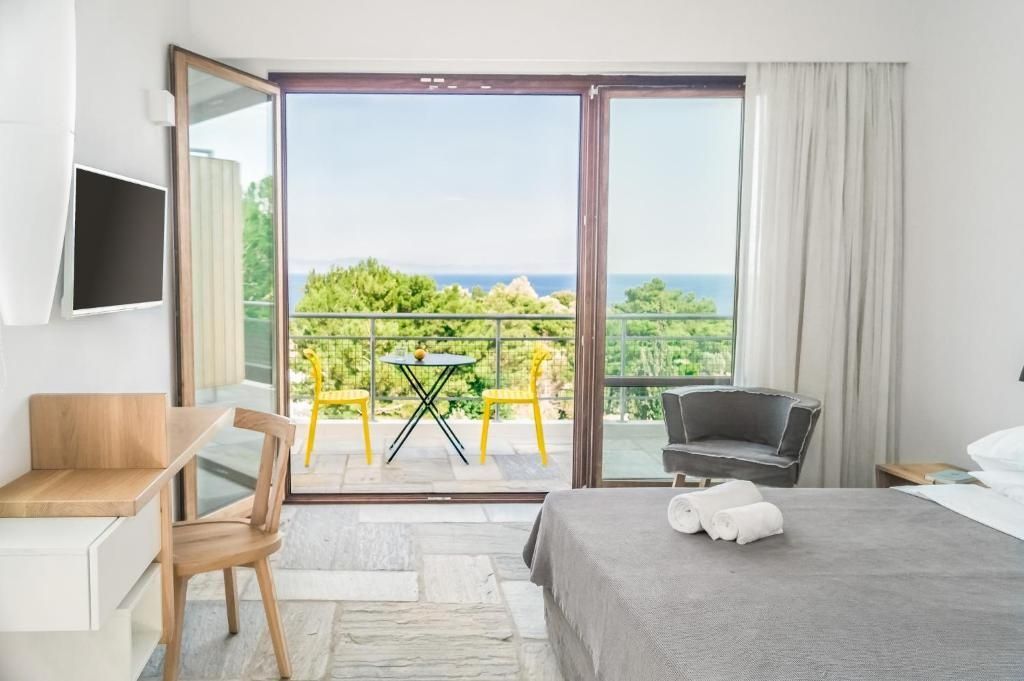 Blick aus dem Hotelzimmer auf eine Terrasse mit gelben Stühlen und das dahinterliegende Meer.