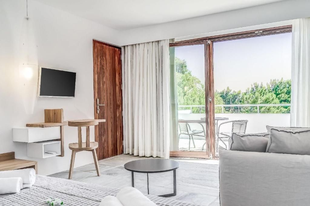 Helles Hotelzimmer mit Holztür, Schreibtisch und Balkonzugang ins Grüne.