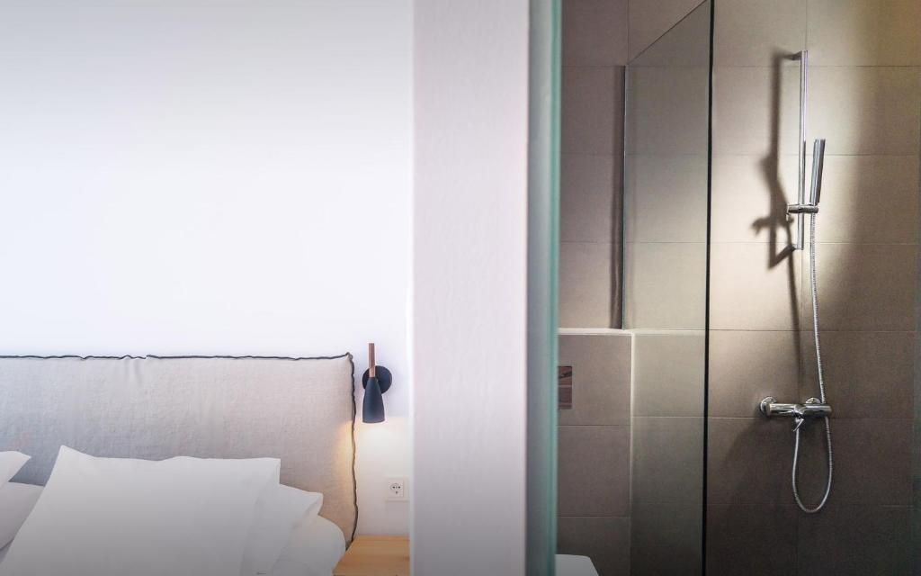 Bett mit beigem Kopfteil und kleiner Wandlampe neben dem Eingang zum hell gefliesten Badezimmer.