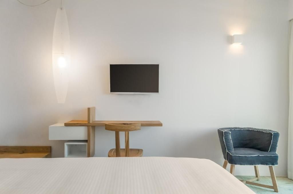 Helles Schlafzimmer mit weißem Bett, Schreibtisch aus Holz und Wandfernseher.