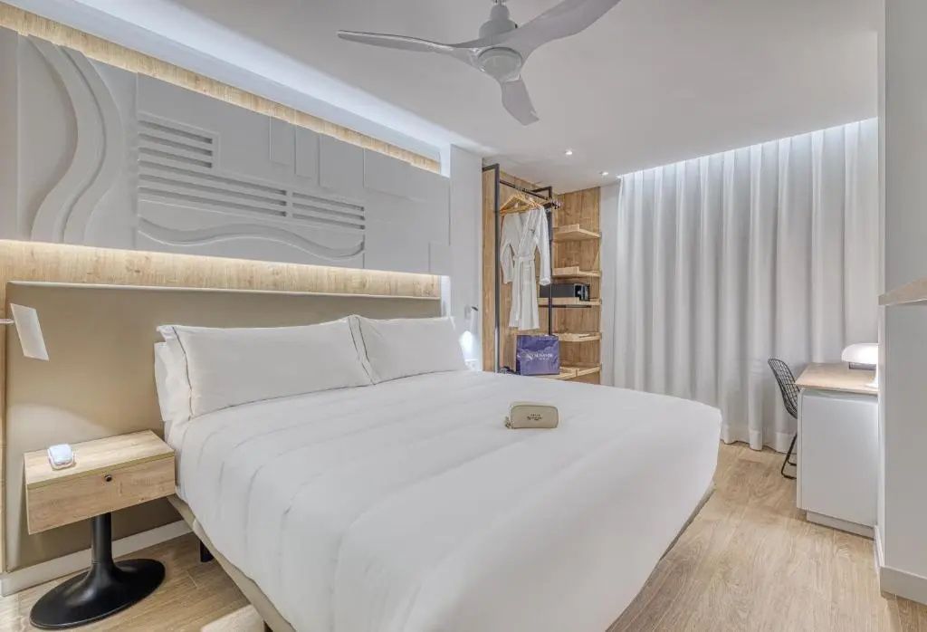 Doppelbett in hellem Hotelzimmer mit Deckenventilator und offenem Kleiderschrank.