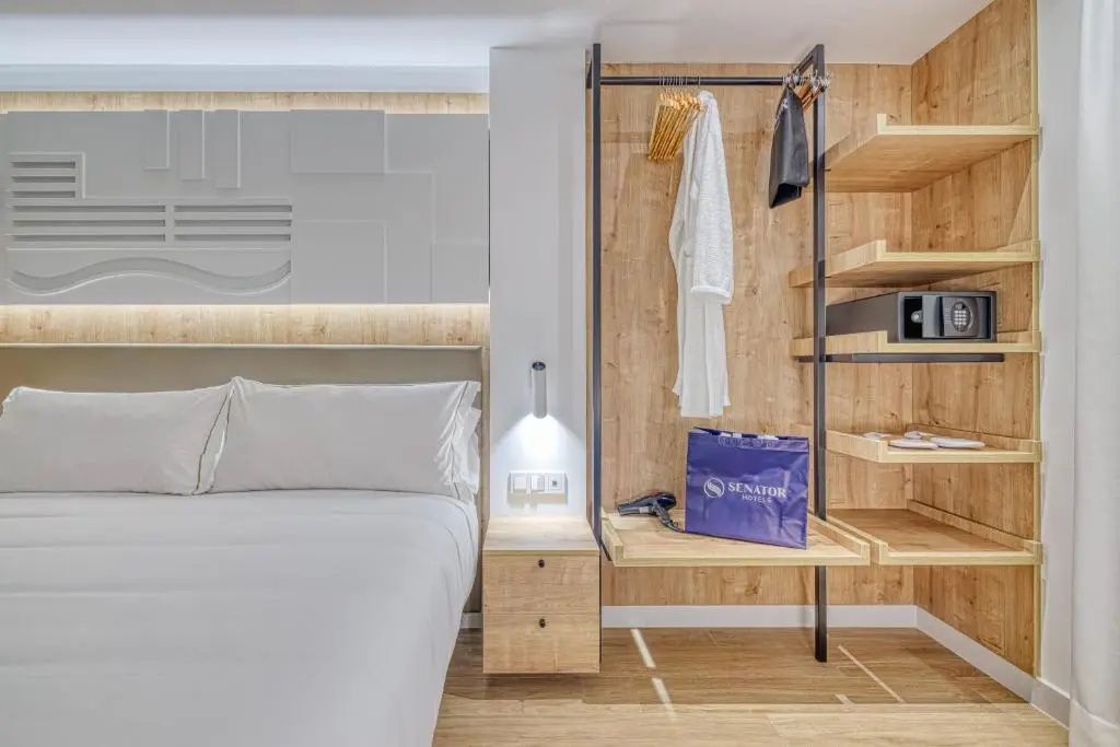 Doppelbett mit weißer Bettwäsche und offenes Holzregal mit Bademantel.