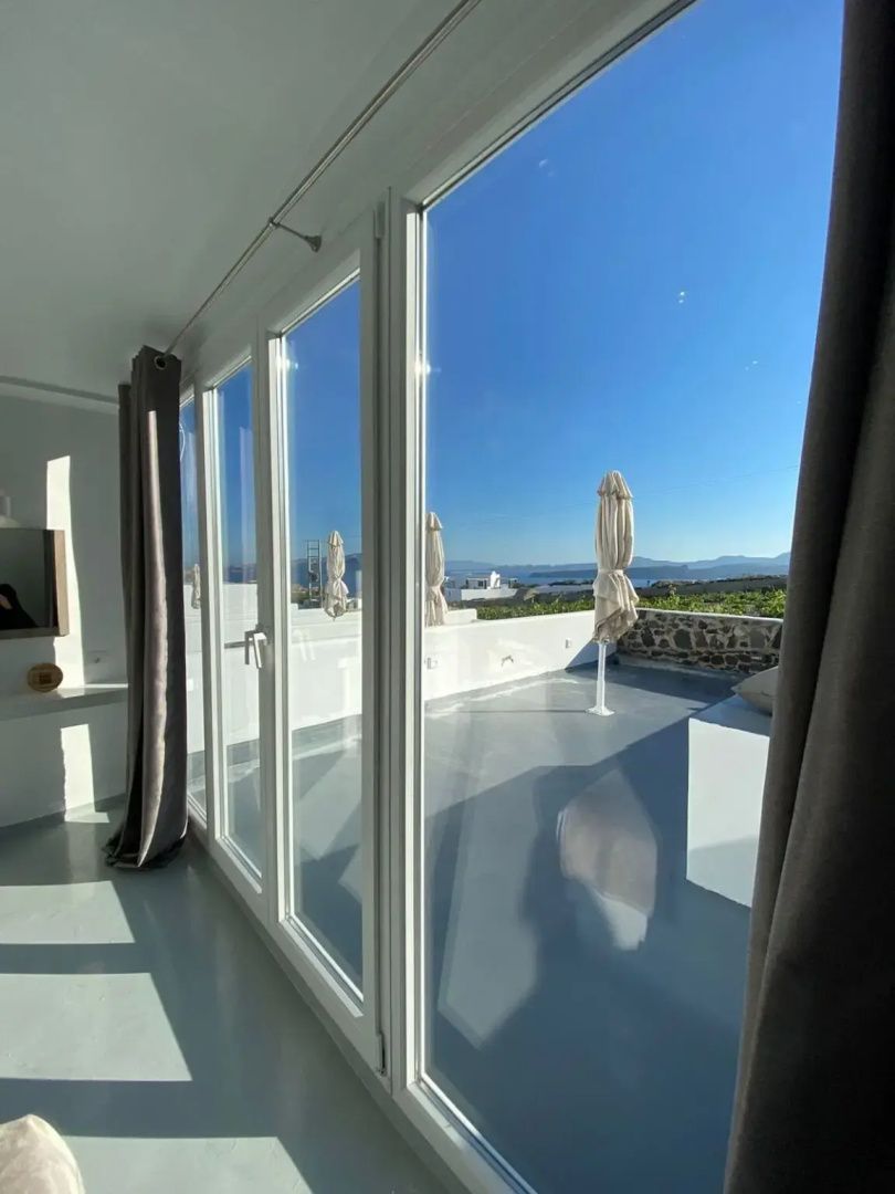 Blick durch die große Glasfront auf eine sonnige Terrasse mit Ausblick auf Landschaft und Meer.