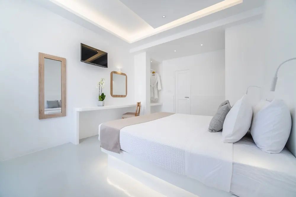 Modernes weißes Schlafzimmer mit Doppelbett, Fernseher, Schminktisch und indirekt beleuchteter Decke.