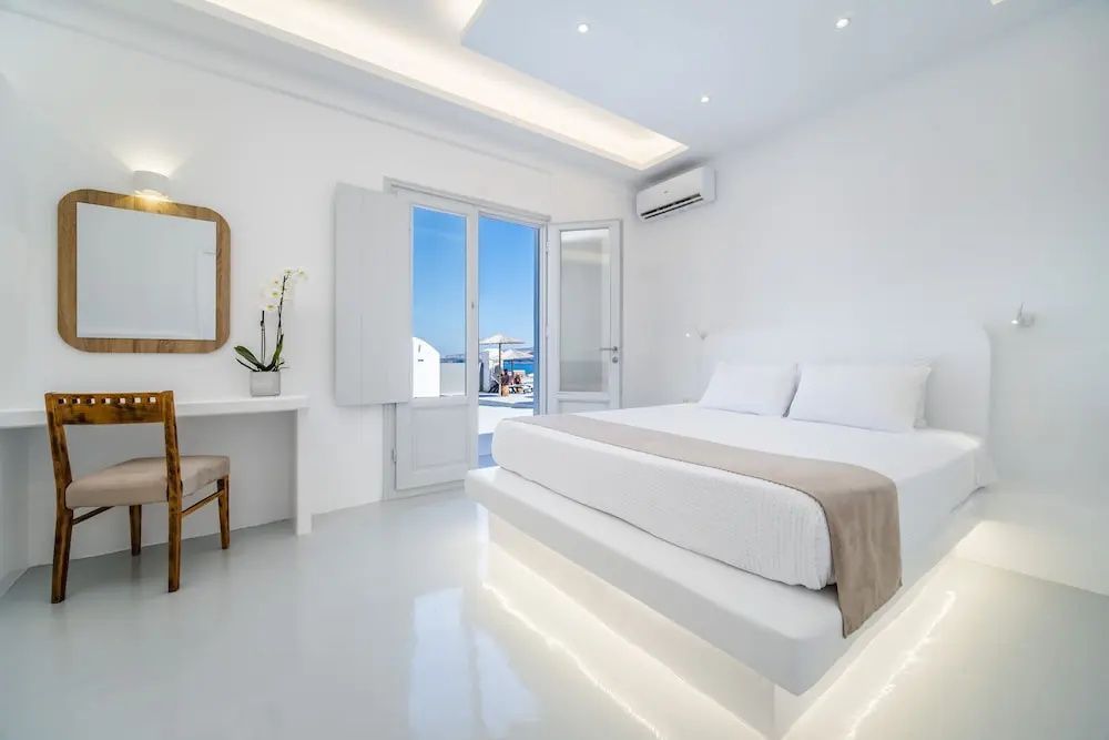 Hell gestaltetes Hotelzimmer mit weißem Bett, Klimaanlage und Zugang zur sonnigen Außenterrasse.