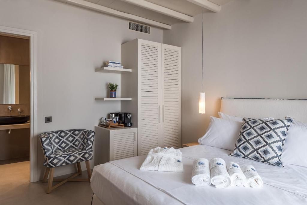 Hell eingerichtetes Schlafzimmer mit Doppelbett, Schrank und gemustertem Sessel.