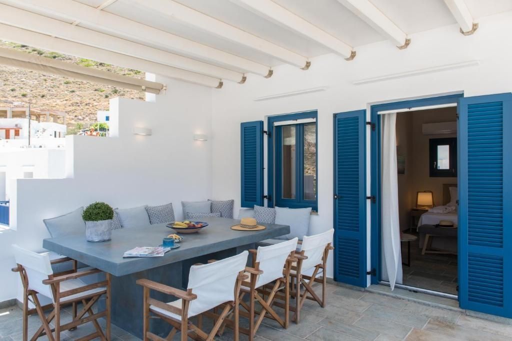 Überdachte Terrasse mit großem Esstisch, weißen Stühlen und blauen Fensterläden.