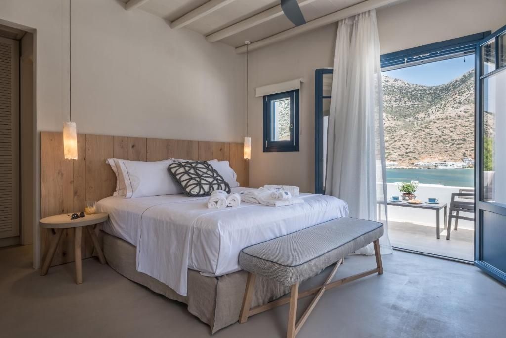 Helles Schlafzimmer mit Doppelbett, gepolsterter Bank und geöffneter Balkontür.