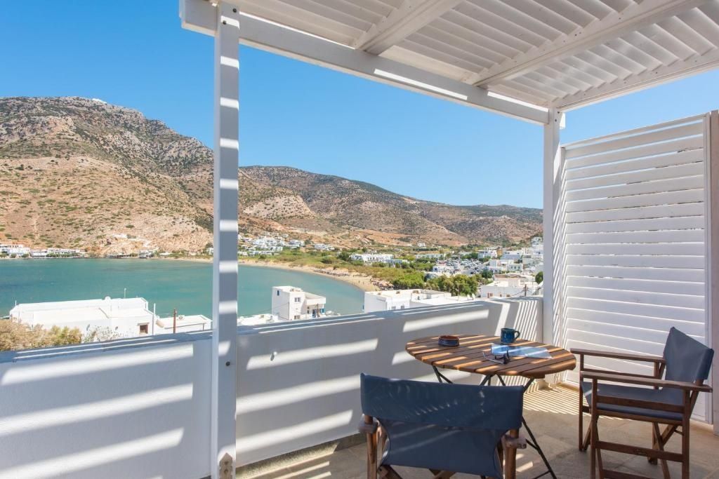 Überdachte Terrasse mit Holzmöbeln und Blick auf eine Meeresbucht und felsige Hügel.