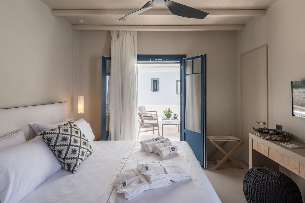 Helles Hotelzimmer mit Doppelbett, Deckenventilator und geöffneter blauer Balkontür