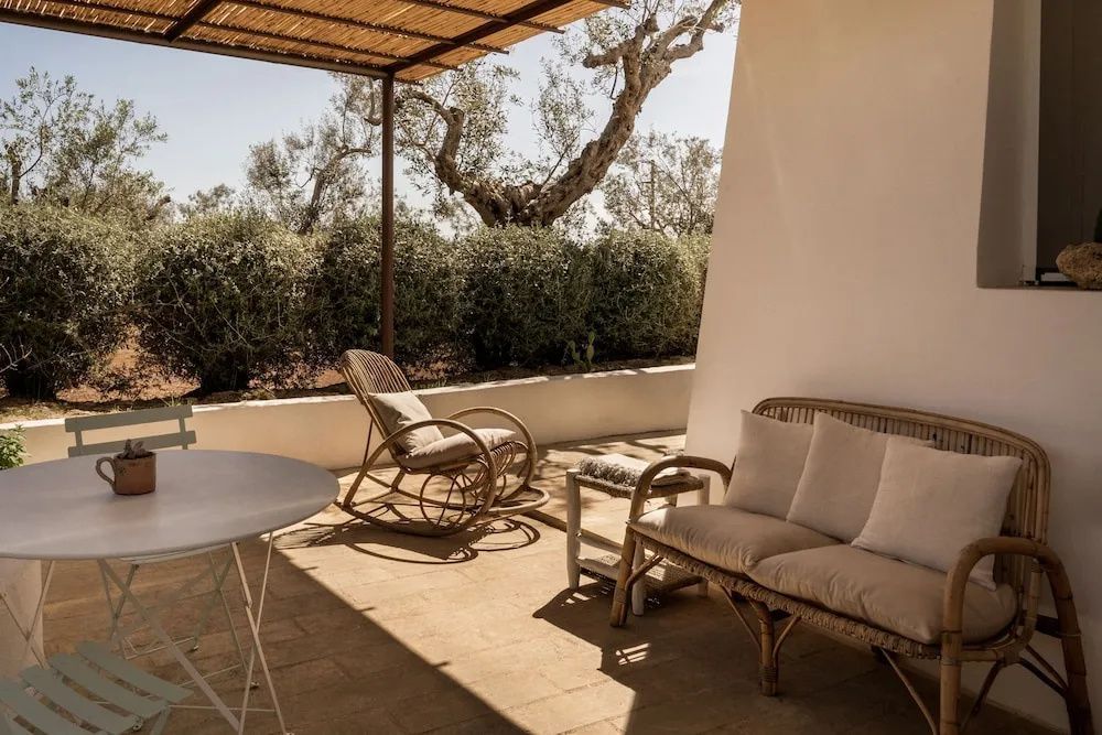 Überdachte Terrasse mit Schaukelstuhl, Sofa aus Geflecht und Blick auf Olivenbäume.