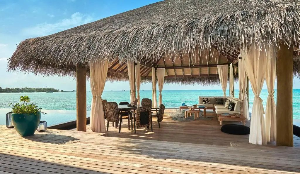 Reetgedeckter Pavillon auf einer Holzterrasse mit Esstisch und Blick auf den Ozean.