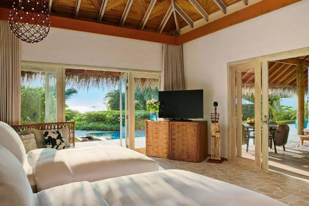 Schlafbereich einer Villa mit Holzdecke, Fernseher und Blick auf Pool und Meer.